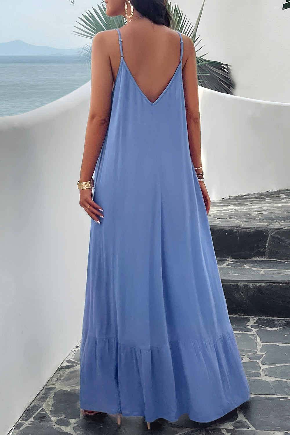 A woman wearing a blue backless maxi cami dress with pockets, standing near a tropical setting.