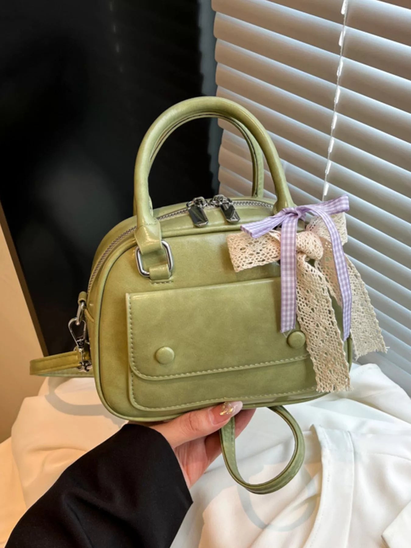 Green handbag with a decorative bow held by a person against a neutral background
