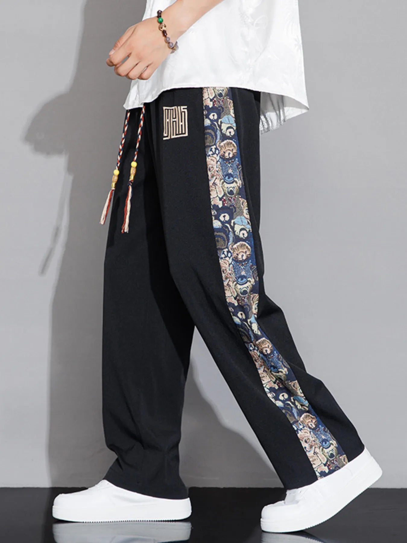 Black pants with colorful side panels worn by a person on a gray background