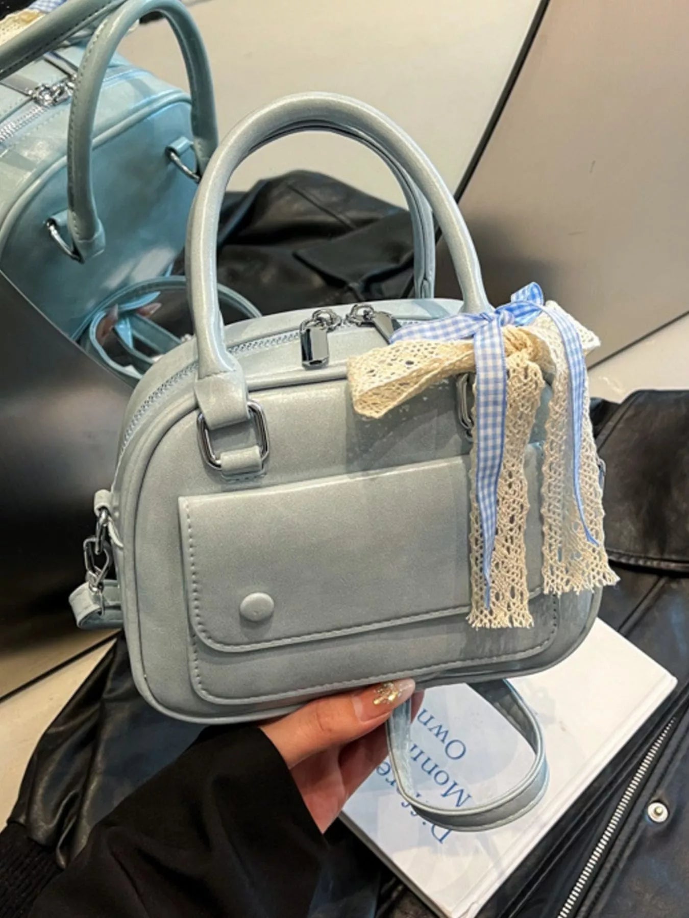 Gray handbag with decorative tassels held by a person, with a blurred background.