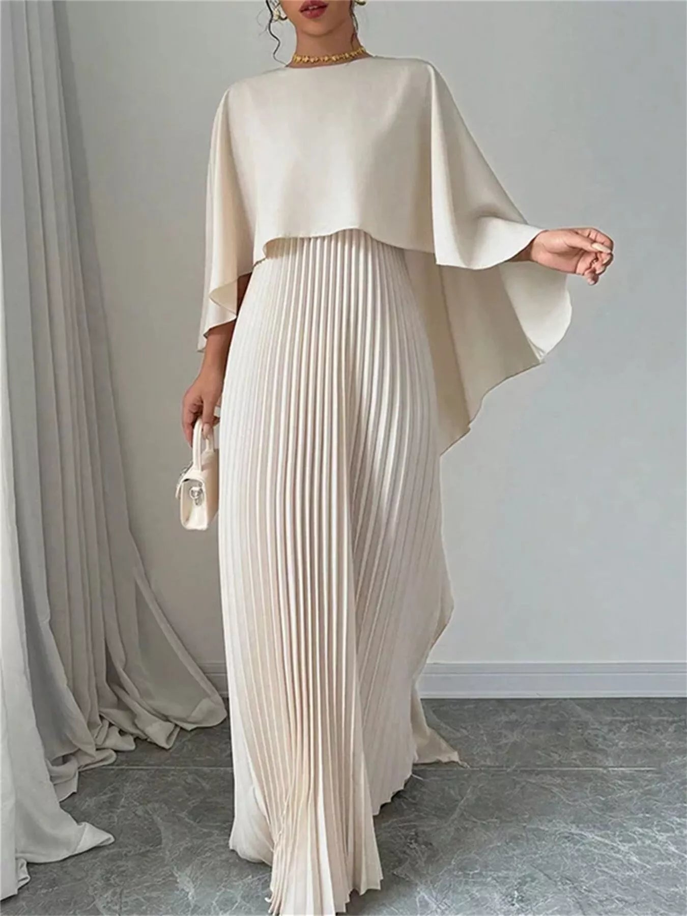 Woman wearing a beige outfit with a draped top and pleated skirt against a plain background