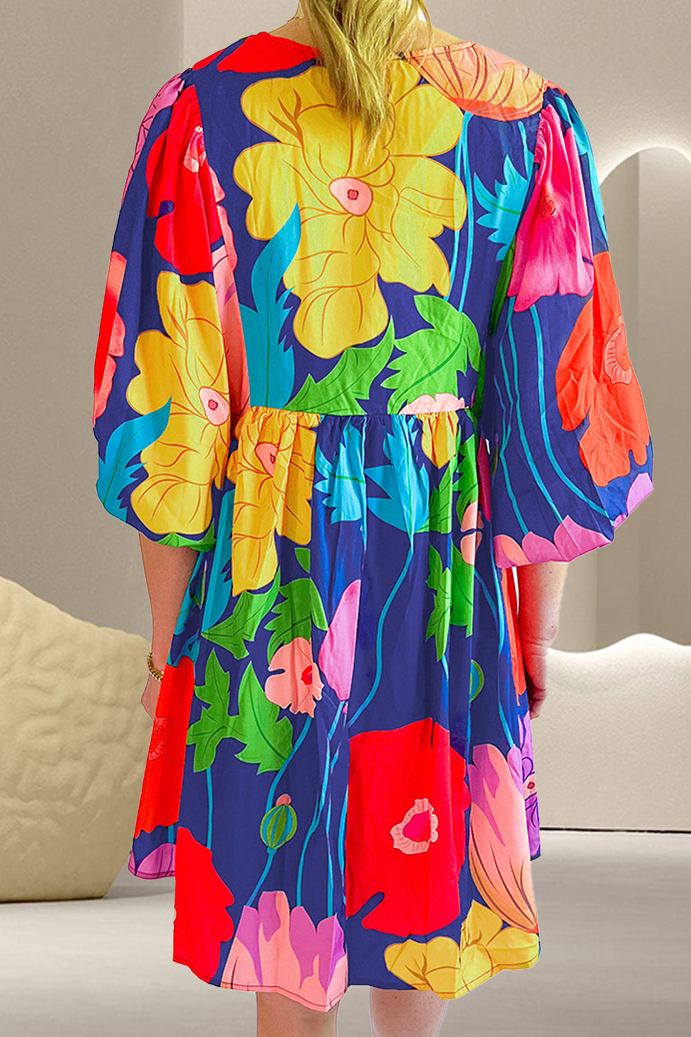 Back view of floral cotton mini dress showing gathered seam, voluminous half sleeves, and colorful print.
