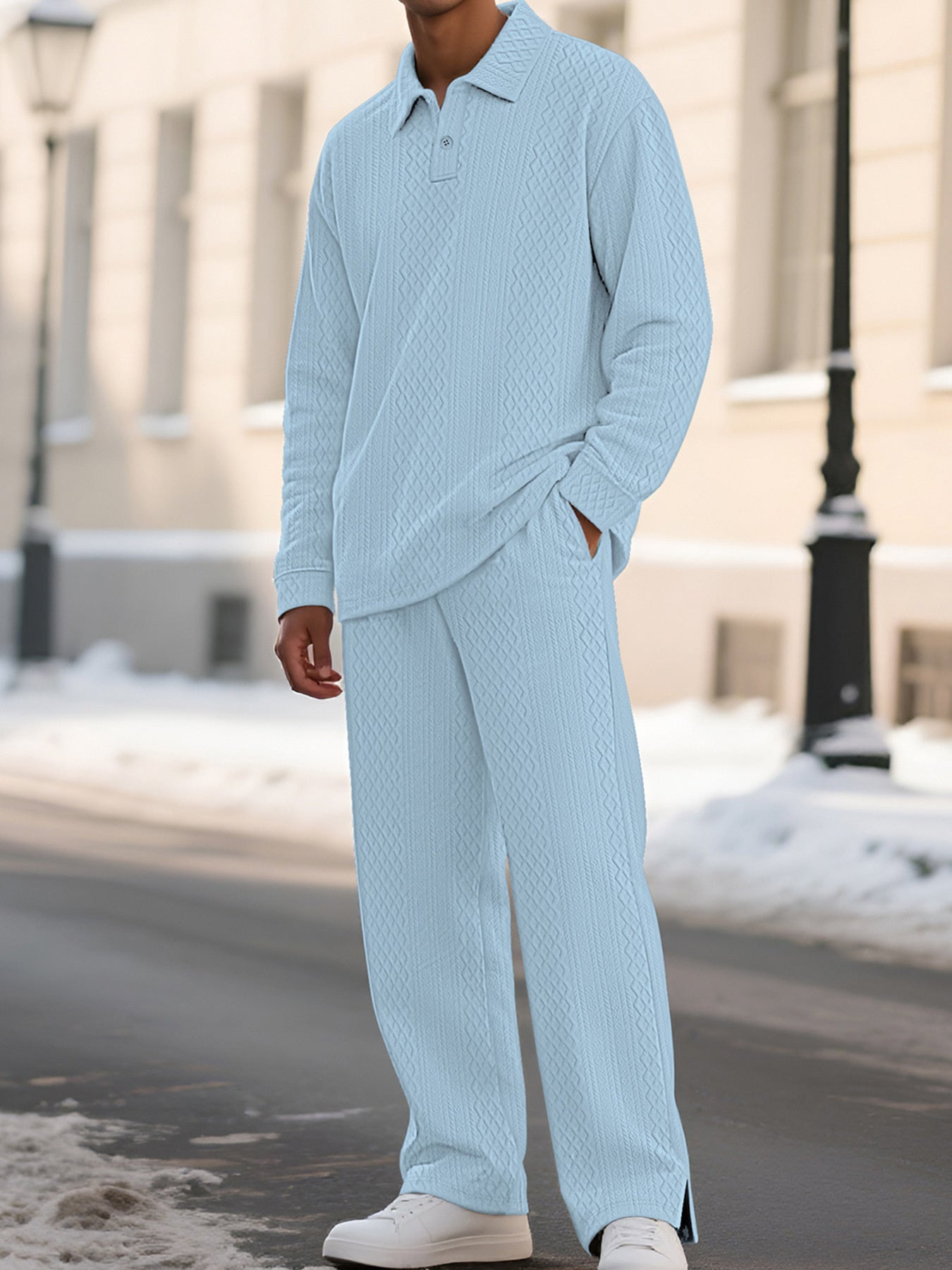 A man wearing a light blue textured knit matching set consisting of a long-sleeve polo shirt and wide-leg trousers, standing outdoors on a snowy street.