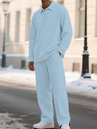A man wearing a light blue textured knit matching set consisting of a long-sleeve polo shirt and wide-leg trousers, standing outdoors on a snowy street.
