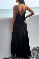 A woman, back view wearing a black backless maxi cami dress with pockets, standing near a tropical setting.