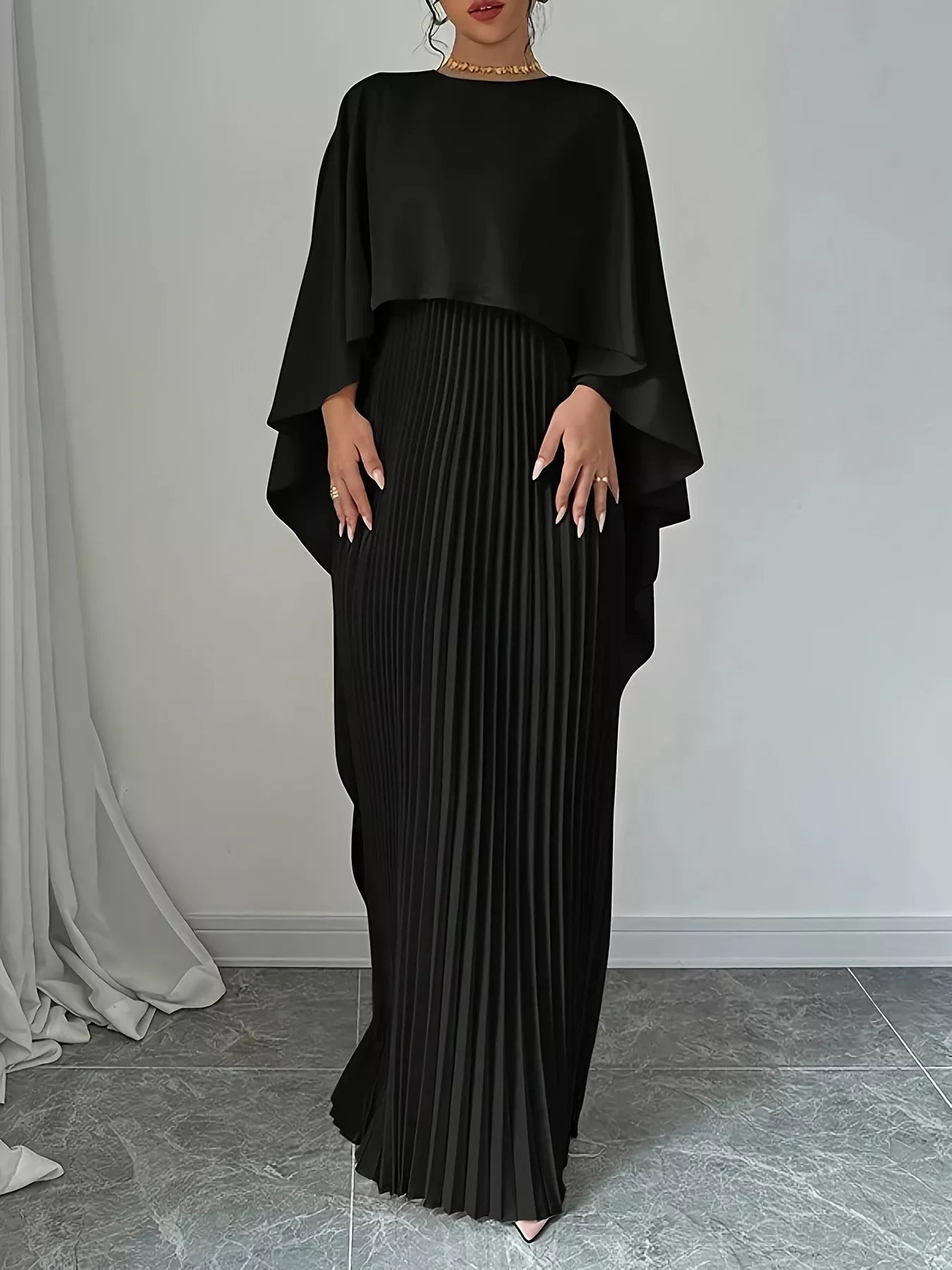 Woman wearing a black pleated dress with a draped top against a neutral background