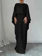 Woman wearing a black pleated dress with a draped top against a neutral background