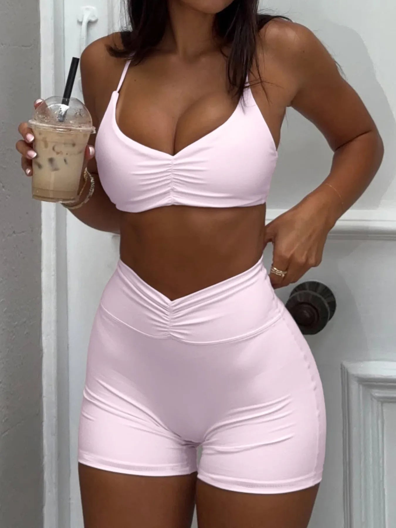 Person wearing a pink sports bra and shorts set, holding an iced coffee.