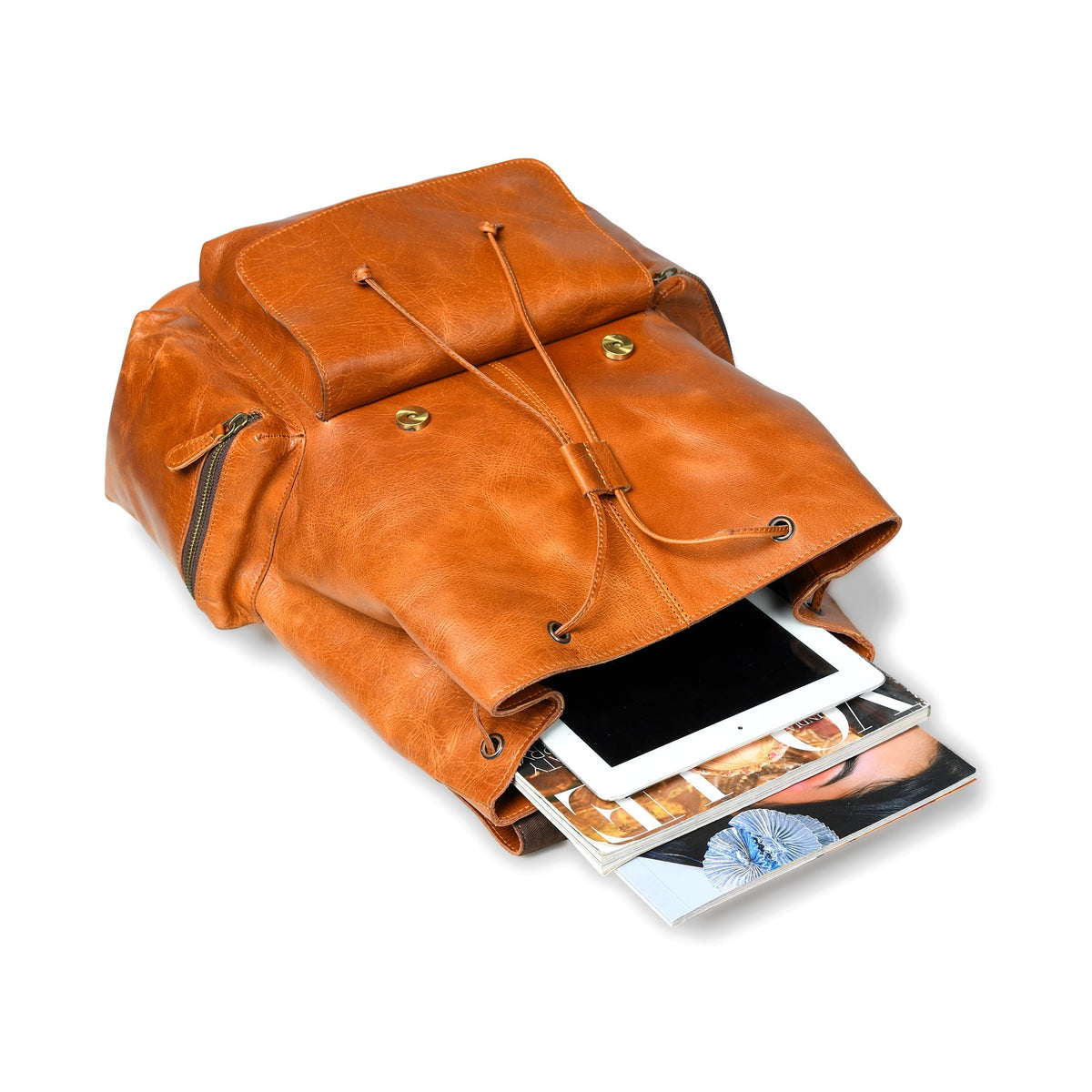Brown leather backpack with a tablet and magazine inside on a white background