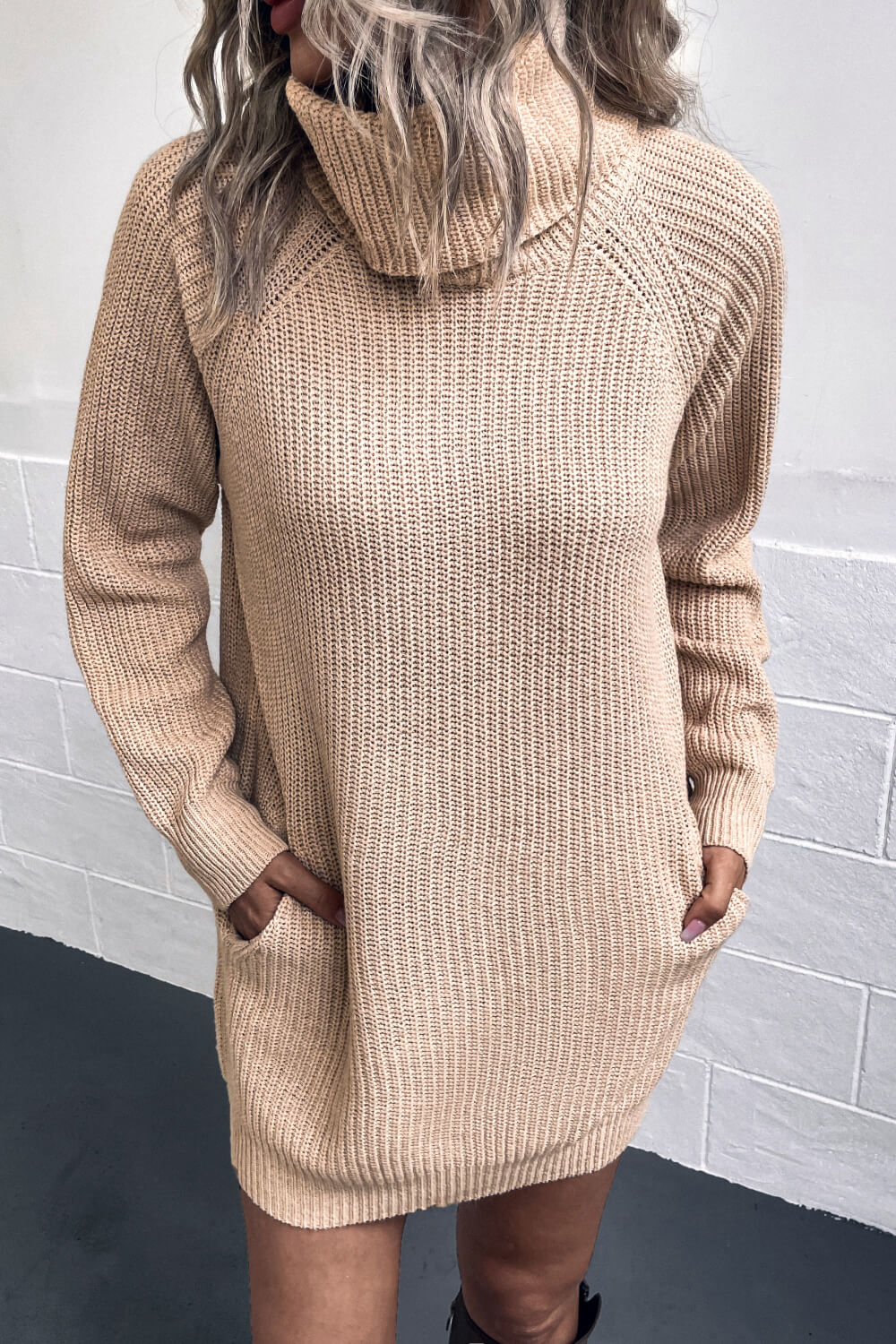 Woman with hands in pockets wearing a Beige turtlenecck sweater dress.