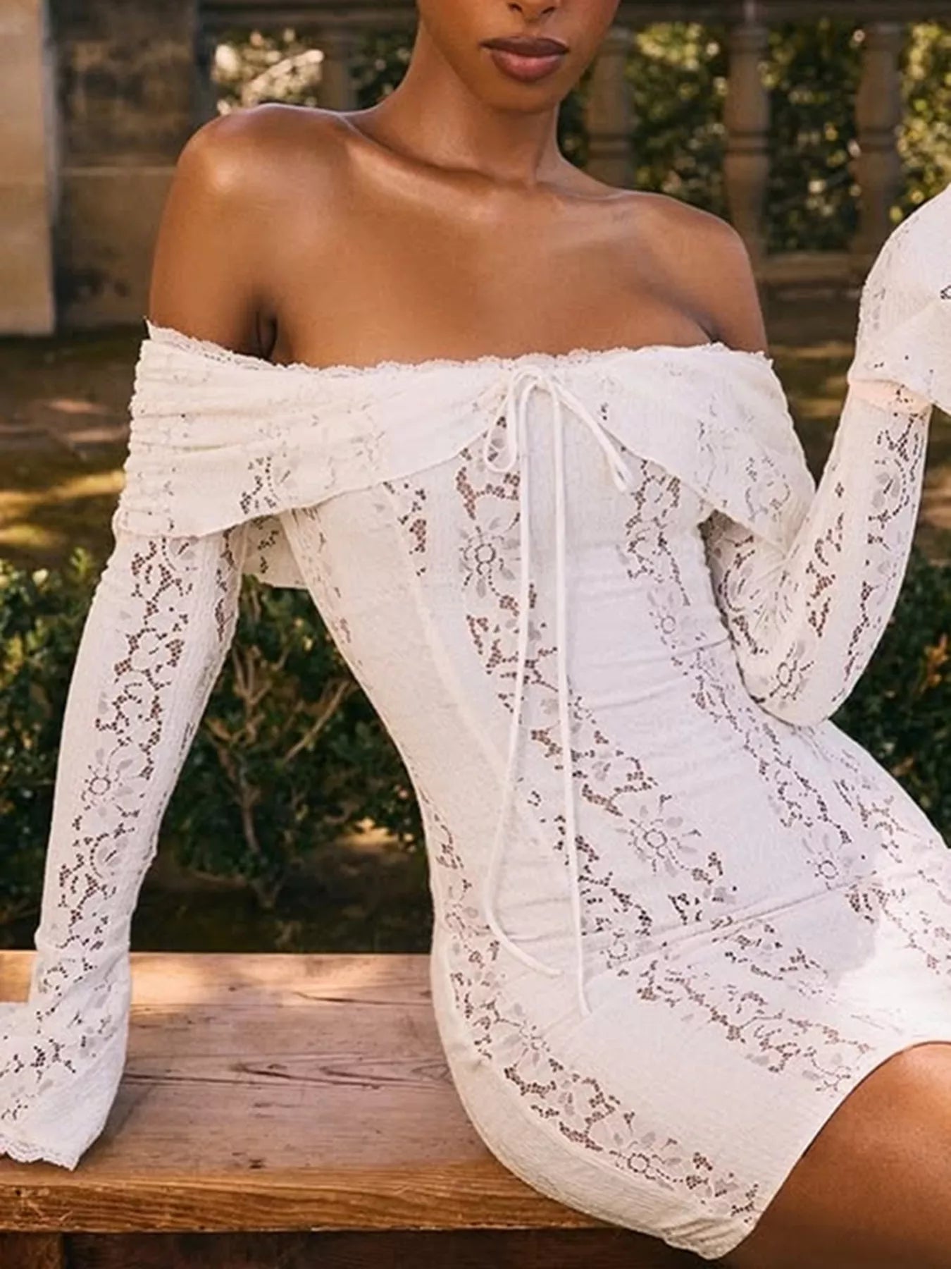 Woman wearing a white lace dress sitting outdoors.