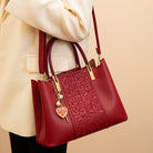 Red handbag with gold accents held by a person wearing a beige coat on a beige background