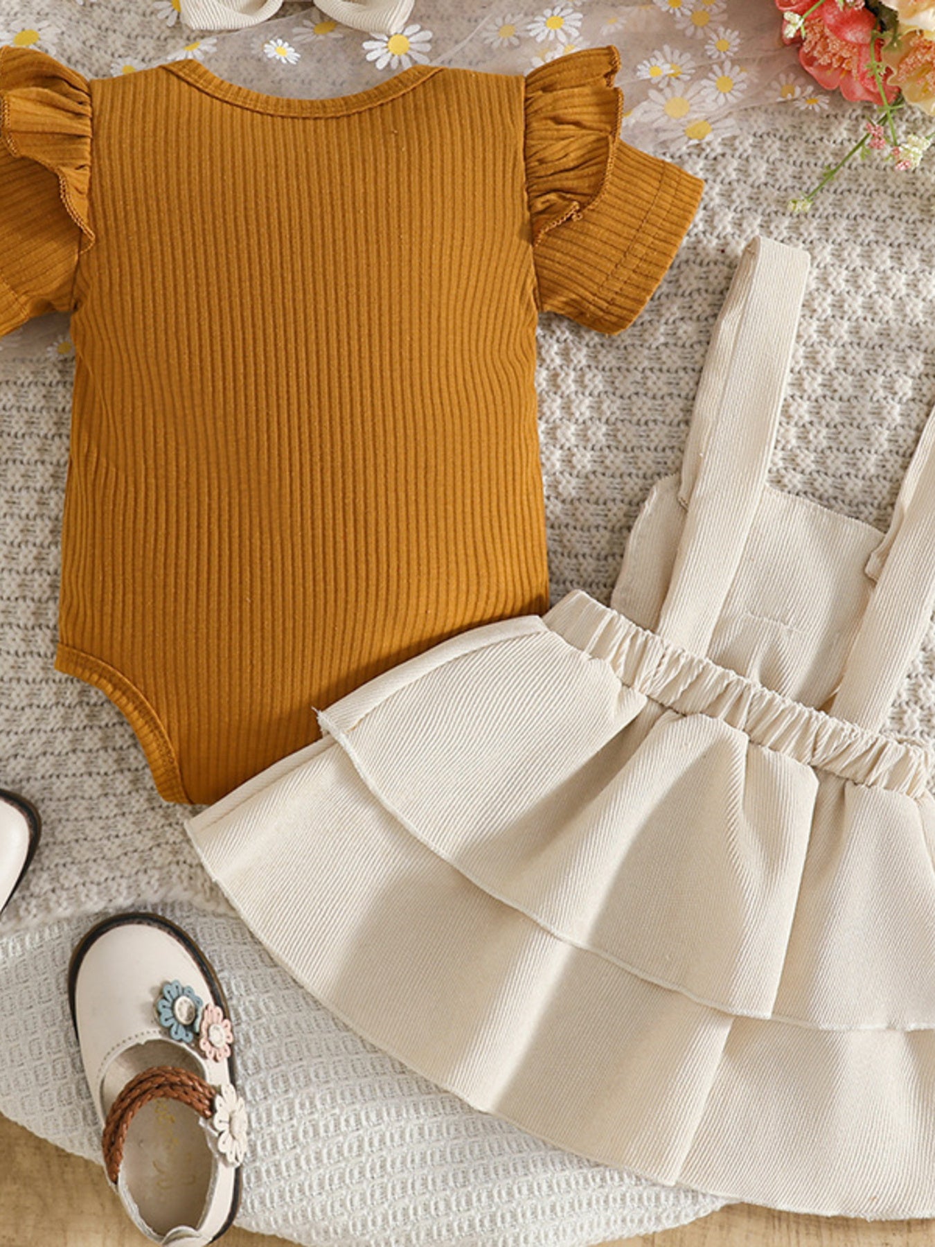 Mustard yellow bodysuit with ruffled sleeves and a white skirt on a textured surface.