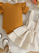 Mustard yellow bodysuit with ruffled sleeves and a white skirt on a textured surface.