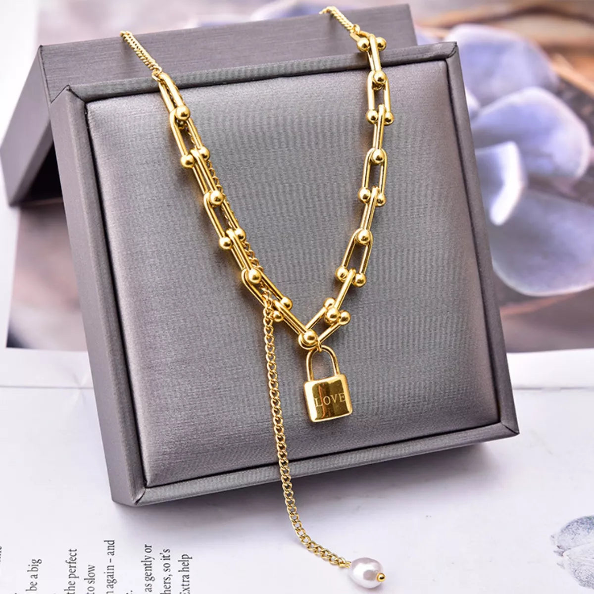Gold chain necklace with a lock pendant on a gray jewelry box