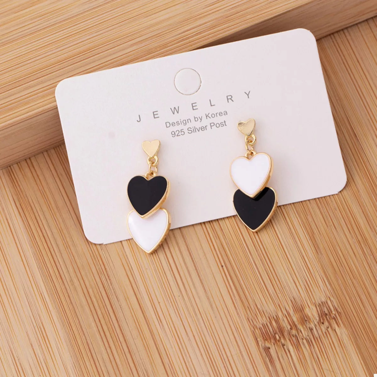 Heart-shaped earrings on a jewelry card with 'Design by Korea' text on a wooden surface.