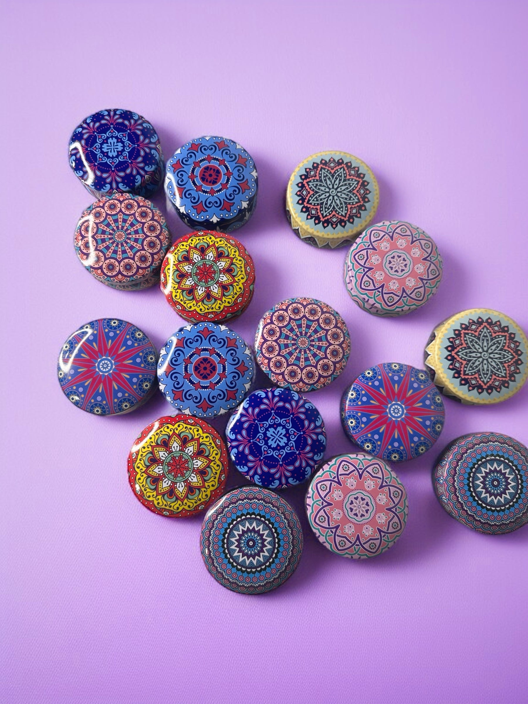Colorful mandala-patterned objects on a purple background. Experience our curated selection of 2 oz tin candles, each crafted with precision in four exceptional fragrance profiles. The Zodiac option combines dark vetiver with sweet sandalwood for a grounding aroma, while Floral delivers the delicate essence of calla lily. Marble offers a crisp sea mist composition, and Mandala blends Bulgarian lavender with sage for a serene atmosphere. As a limited release collection.