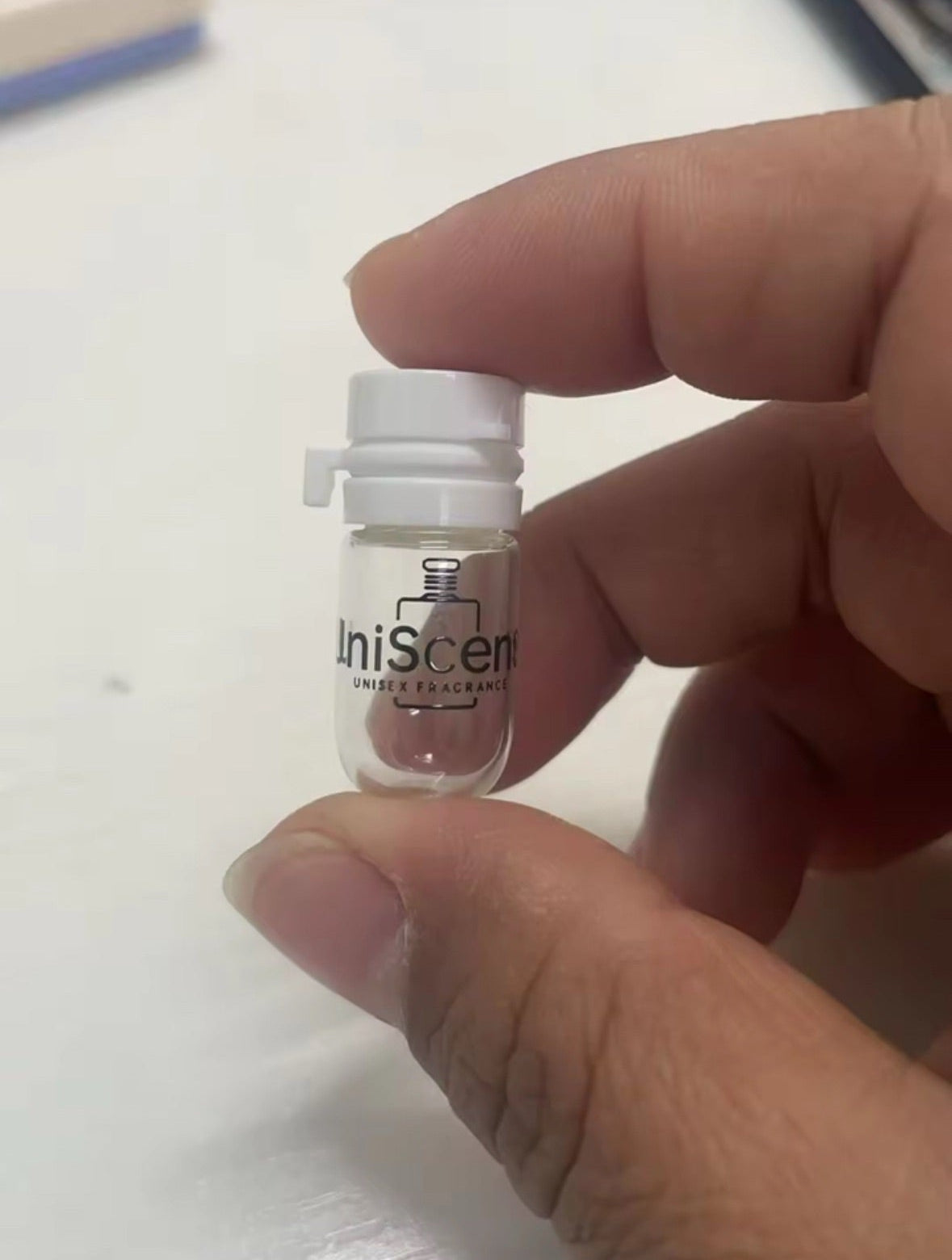 Hand holding a small bottle labeled 'uniScent' against a light background
