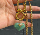 Green aventurine heart pendant necklace with a gold-tone starburst detail and chunky chain held in a hand.