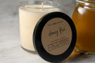 Candle labeled 'Honey Bee' with a jar of honey on a light background. Limited Edition Honey Bee Candle with a warm, golden honey scent. This expertly crafted candle delivers rich, comforting aromas that evoke natural meadows and blooming flowers. Enjoy hours of consistent, high-quality fragrance that brings inviting warmth to any room.