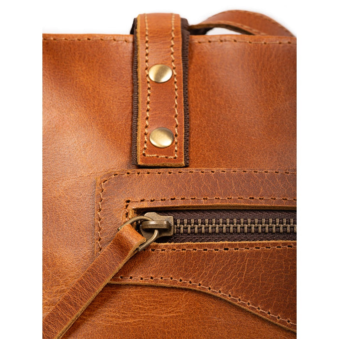 Close-up of the Kodiak tan leather tote showing the exterior zipper, leather pull, brass rivets, and stitching.