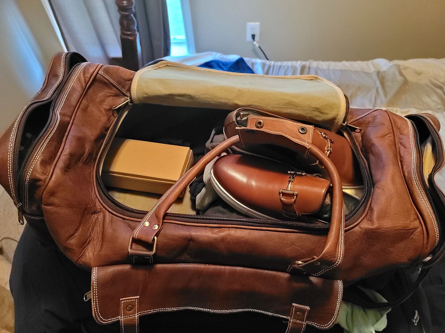 Brown leather duffel bag with items inside on a bed