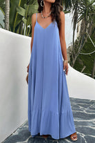 A woman wearing a blue backless maxi cami dress with pockets, standing near a tropical setting.