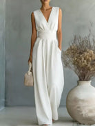 Woman wearing a white sleeveless dress standing in a room with a vase and dried plants.