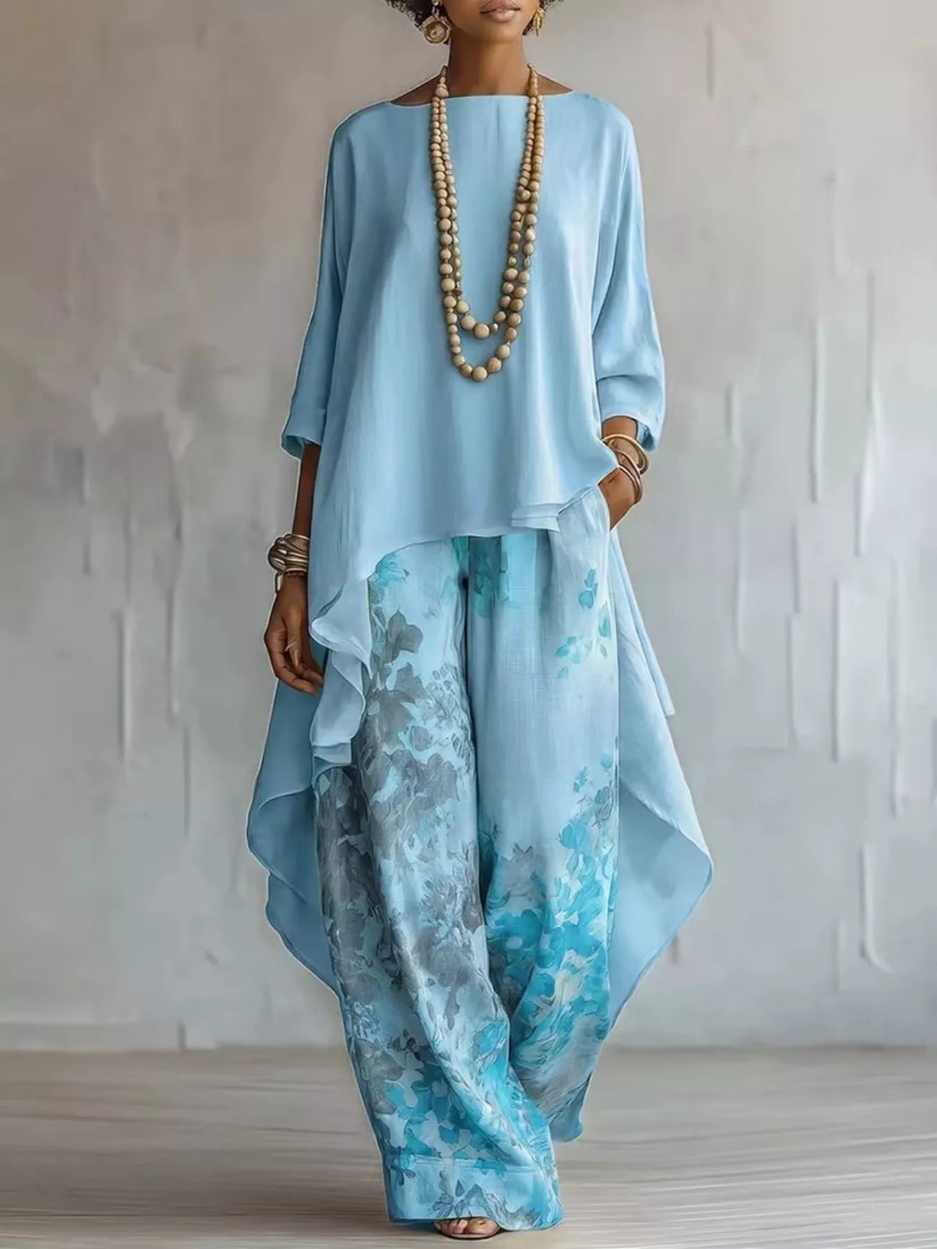 Woman wearing a light blue outfit with a long top and patterned pants against a plain background