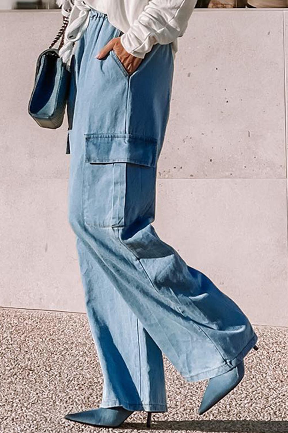 A pair of blue wide leg drawstring jeans with pockets, displayed on a person showing side view against a neutral background.