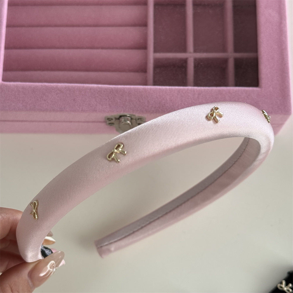 A premium light pink padded spa headband featuring a delicate gold alloy bow trim accent.