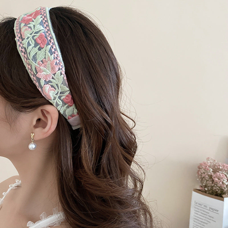 A premium light green padded spa headband featuring delicate, intricate floral embroidery details displayed in a luxury resort style setting.