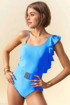 Woman wearing a blue swimsuit with ruffled shoulders against a beige background