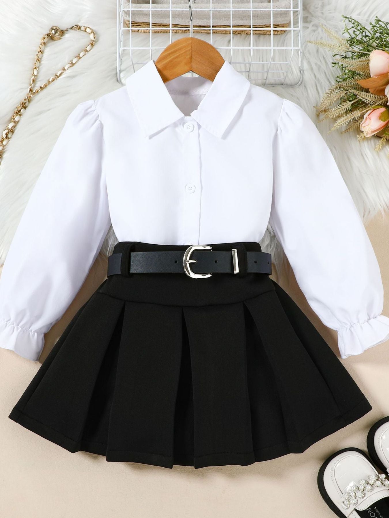 White shirt with black pleated skirt on a beige surface