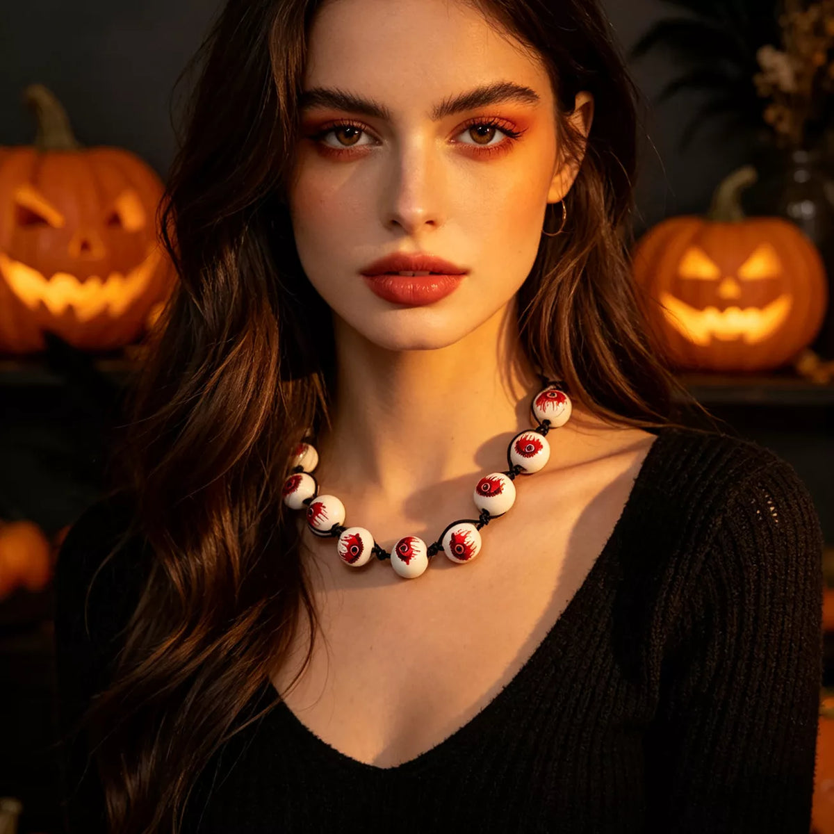 A woman with long dark hair and warm-toned makeup wears a chunky beaded necklace made of white beads with red and black details, posed in front of glowing jack-o'-lanterns.