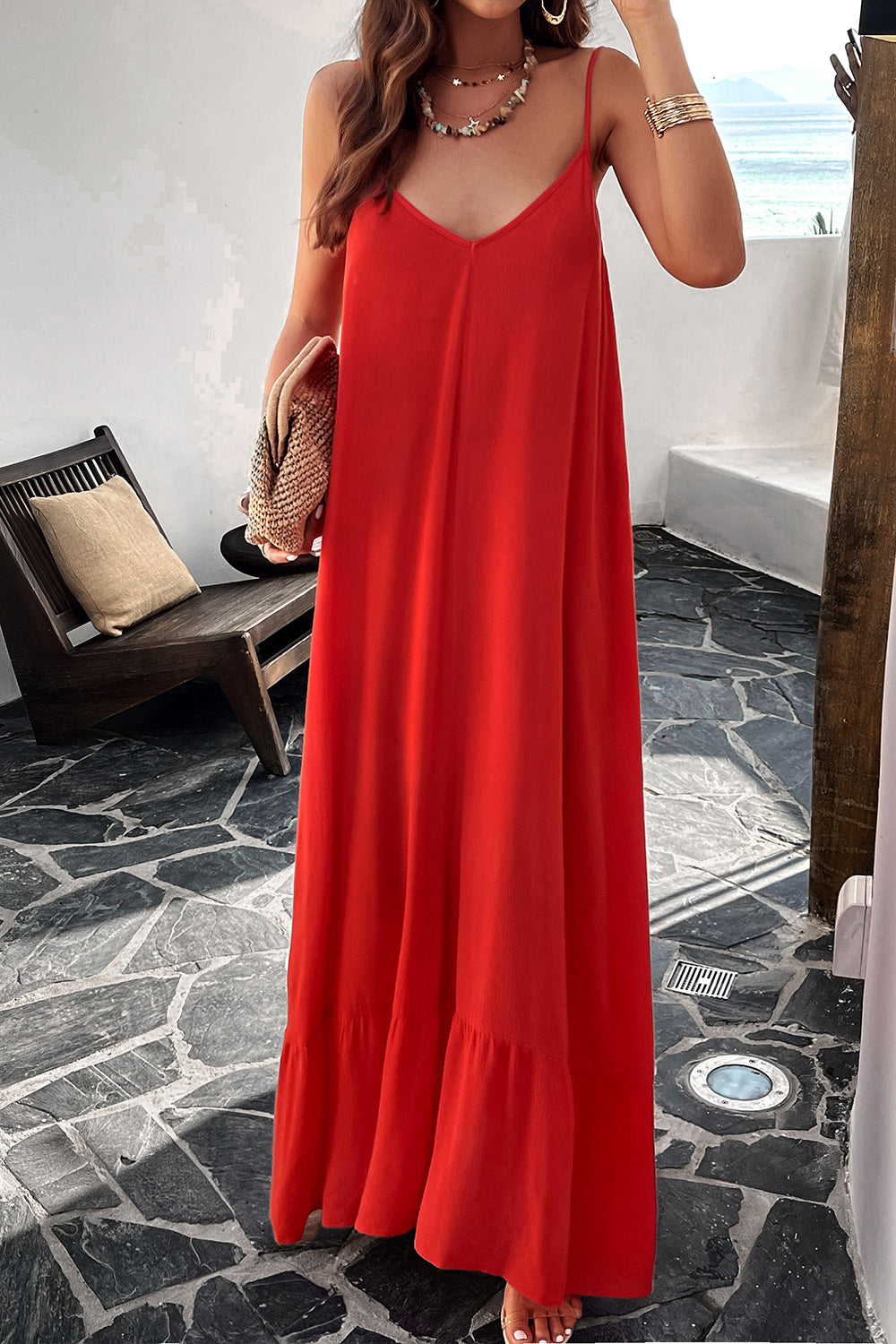 A woman wearing a red backless maxi cami dress with pockets, standing near a tropical setting.