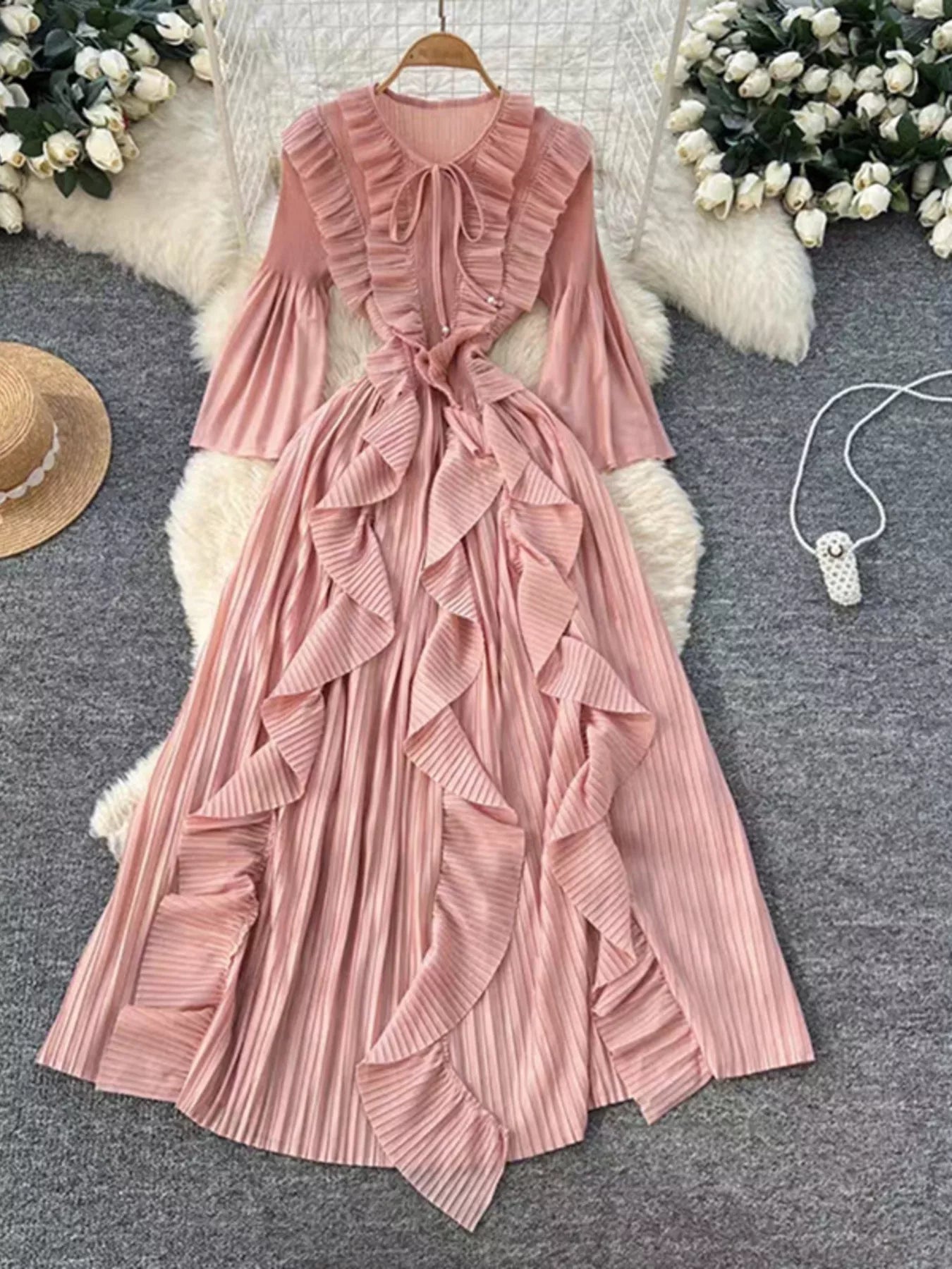 Pink ruffled dress on a hanger with decorative elements on a textured surface.