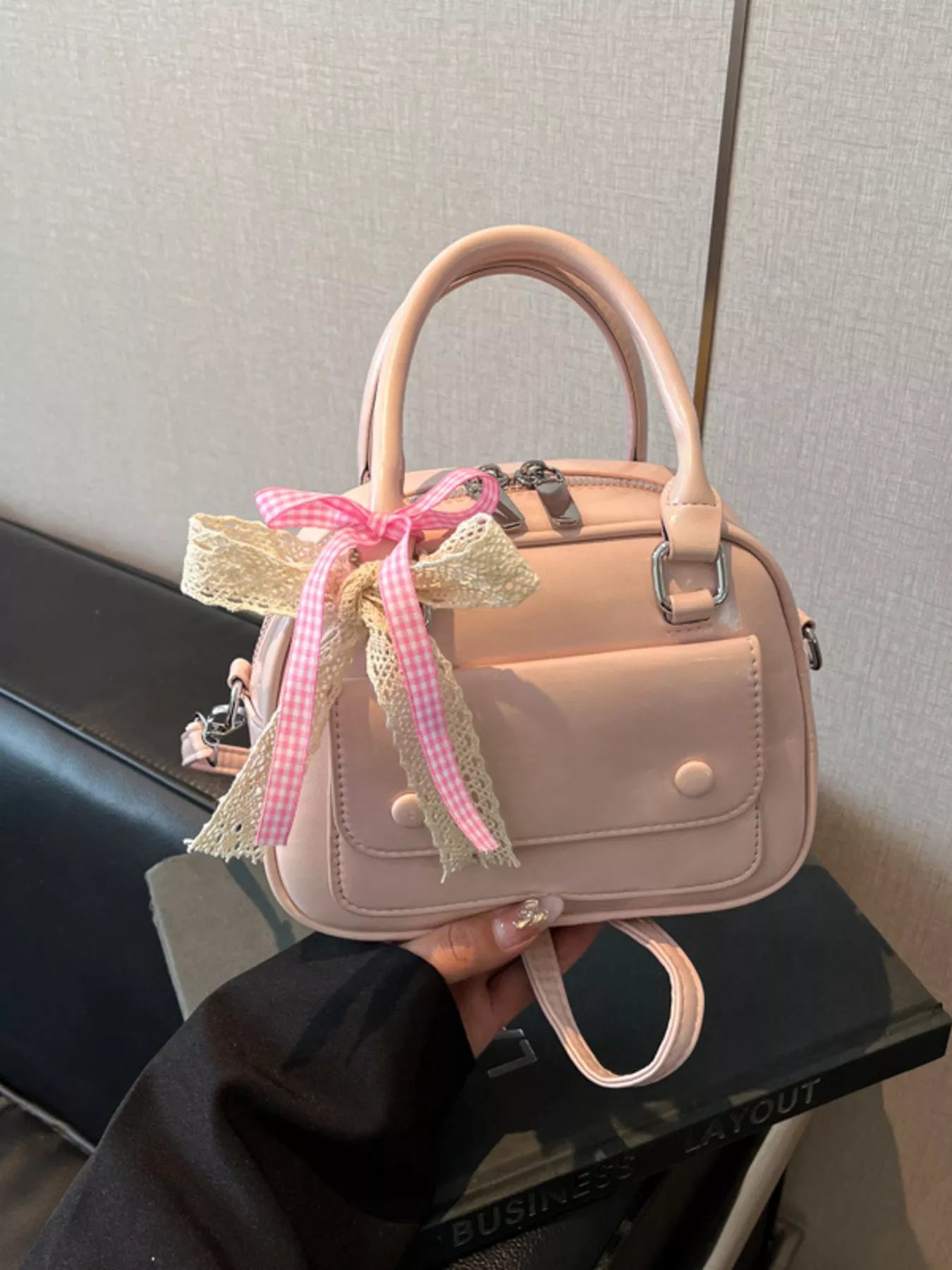 Pink handbag with a decorative bow held by a person against a neutral background