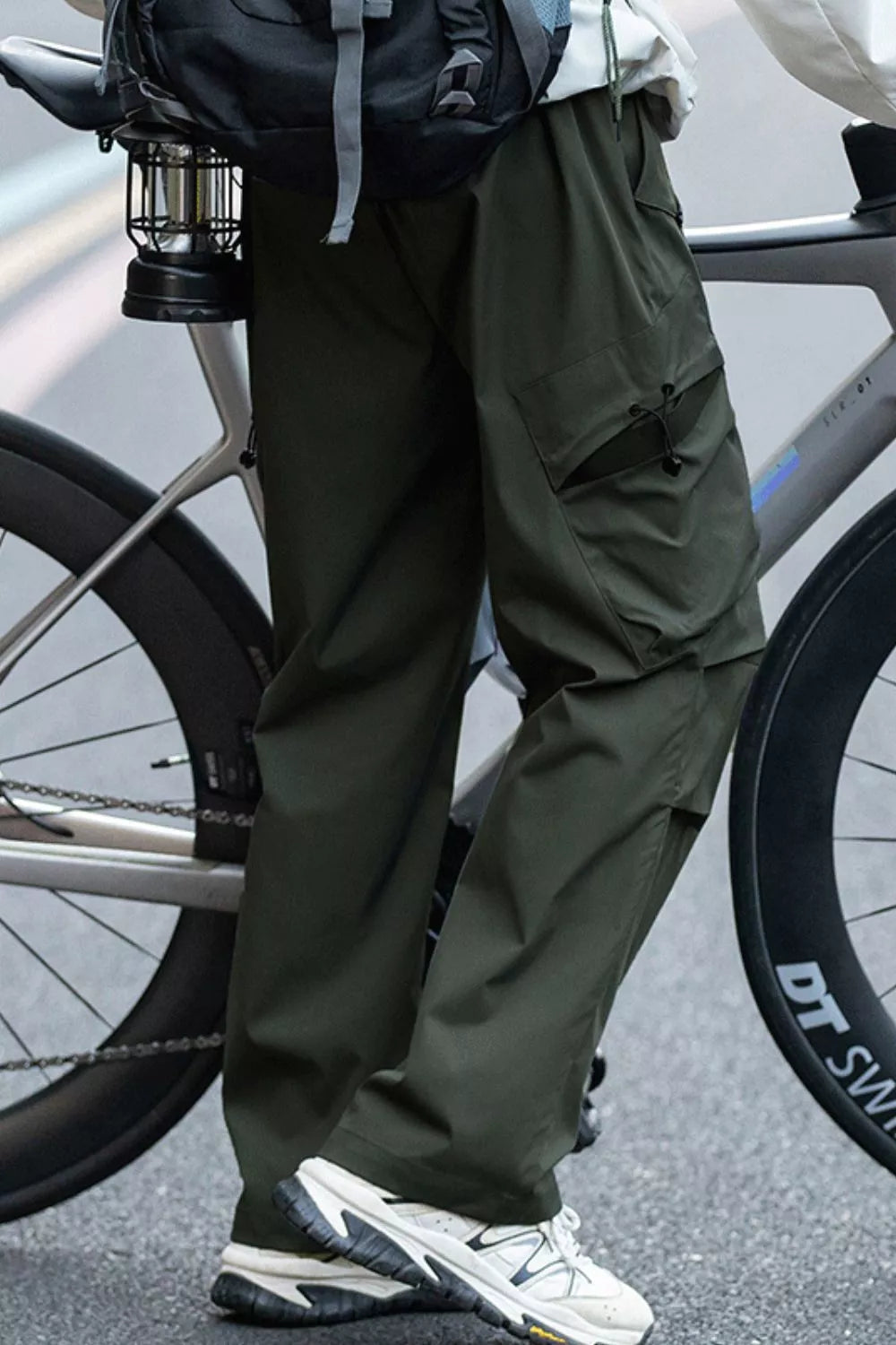 Person wearing green pants and white sneakers standing next to a bicycle on a road.