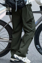 Person wearing green pants and white sneakers standing next to a bicycle on a road.