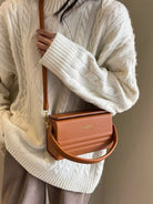 Person wearing a beige sweater holding a brown handbag with 'ALANUI' branding.