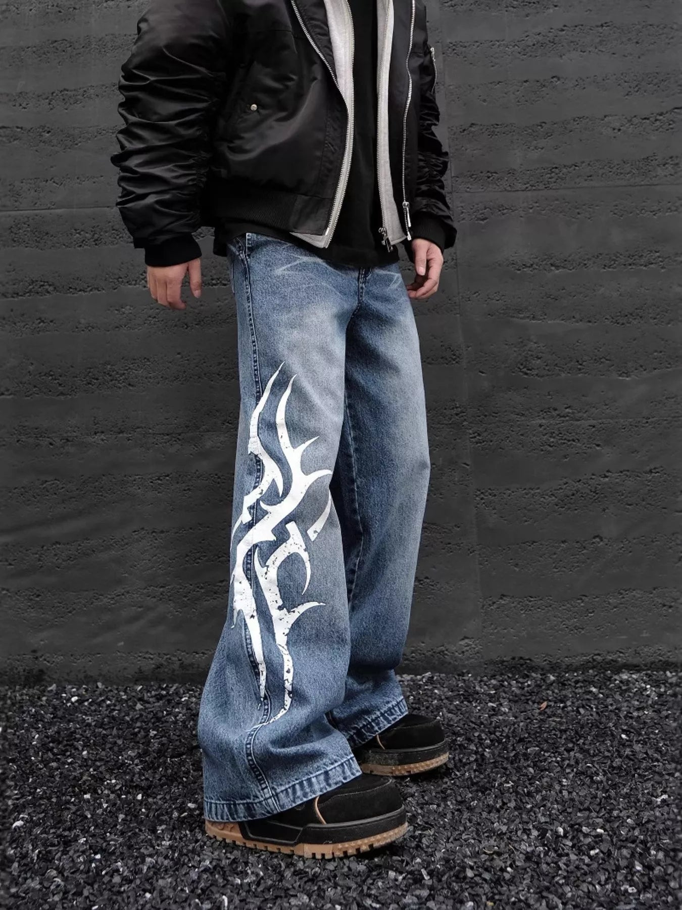 Person wearing blue jeans with a white tribal design against a gray wall.