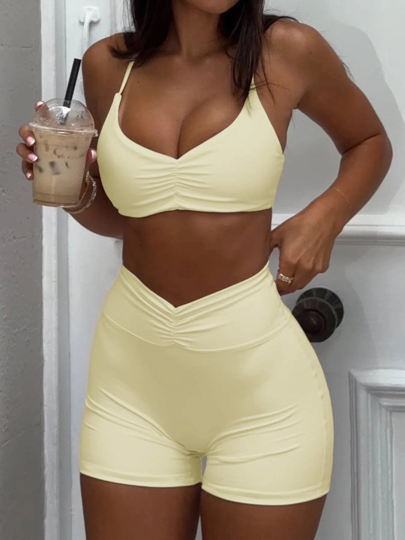 Person wearing a light yellow sports bra and shorts set, holding an iced coffee.