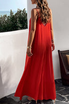 A woman, backless view wearing a red backless maxi cami dress with pockets, standing near a tropical setting.