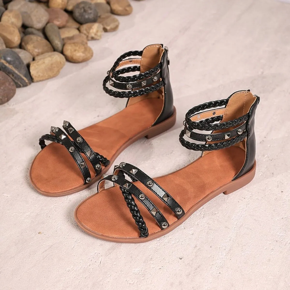 Pair of brown sandals with black straps on a textured surface.