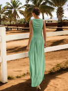 Woman in a green dress standing in a rural setting with palm trees and a white fence.