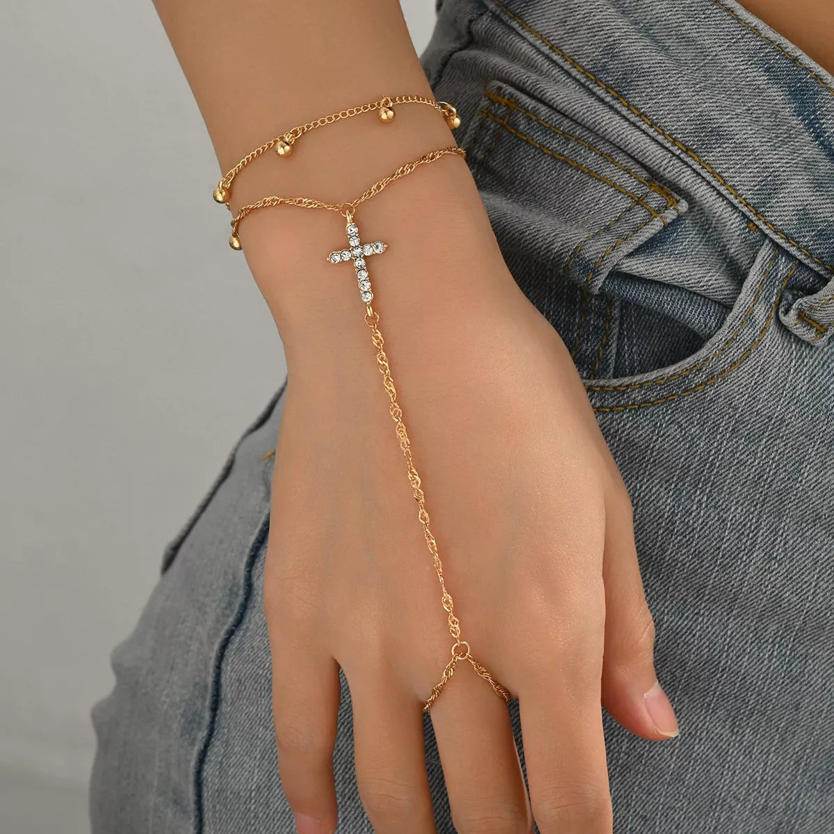Gold bracelet with a cross design on a hand against a gray background