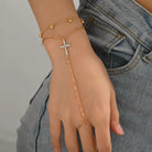 Gold bracelet with a cross design on a hand against a gray background