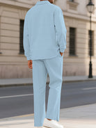 A man wearing a light blue textured two-piece lounge set with a long-sleeve shirt and matching trousers, standing on a city sidewalk.
