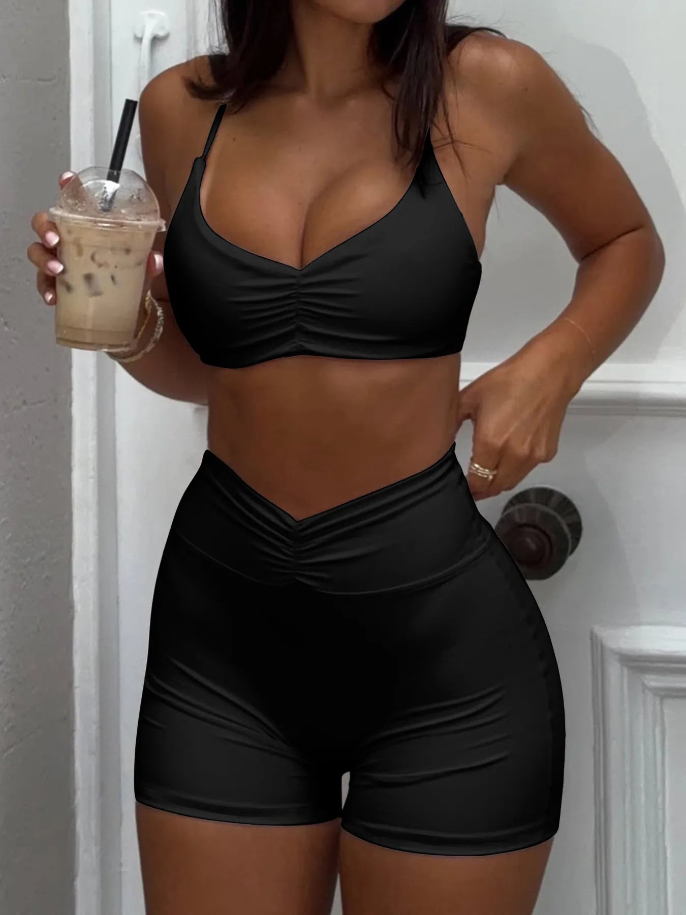Person wearing a black sports bra and shorts holding an iced coffee.